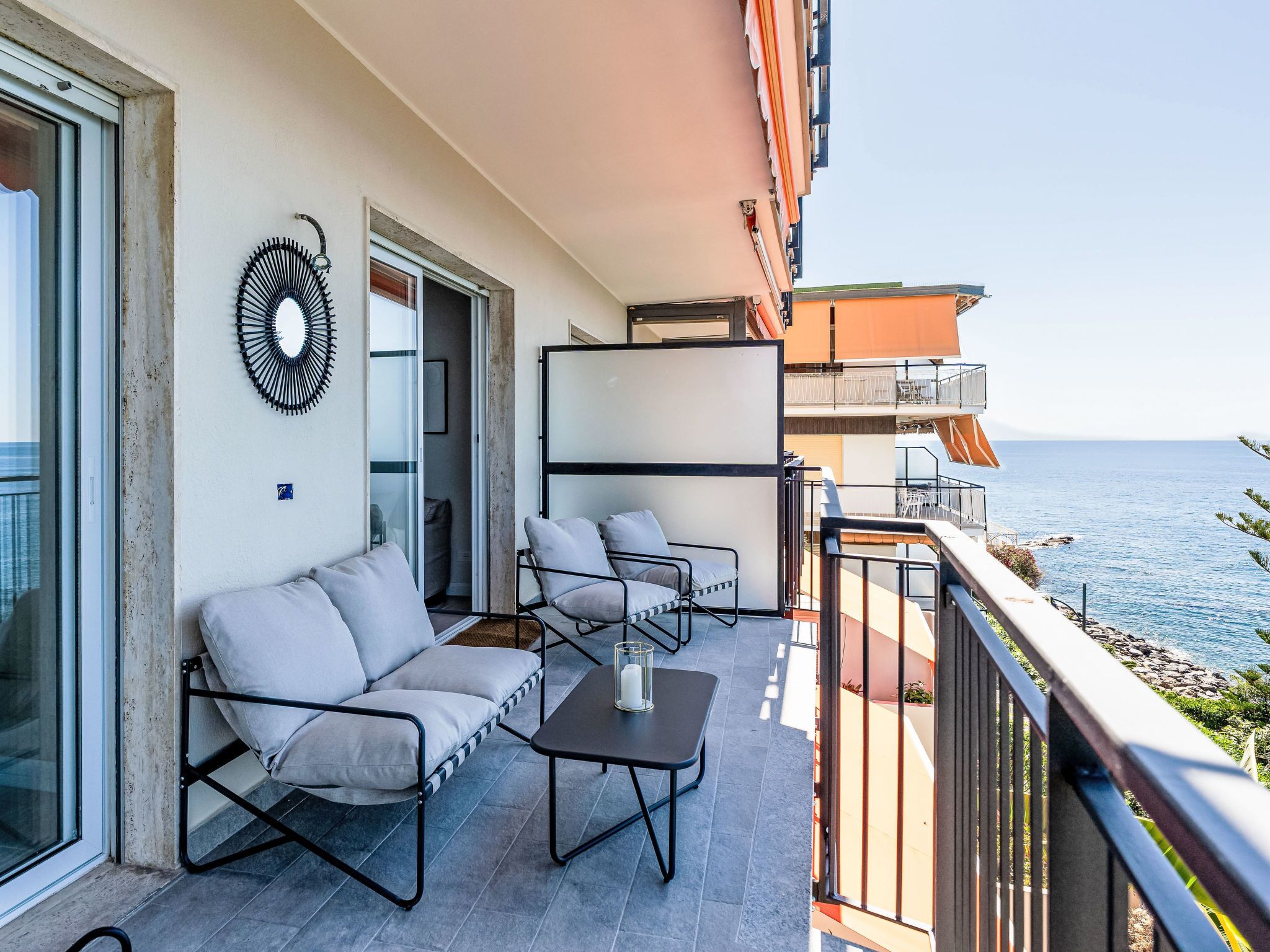 Un balcone con un divano, due sedie, un tavolino e vista mare.