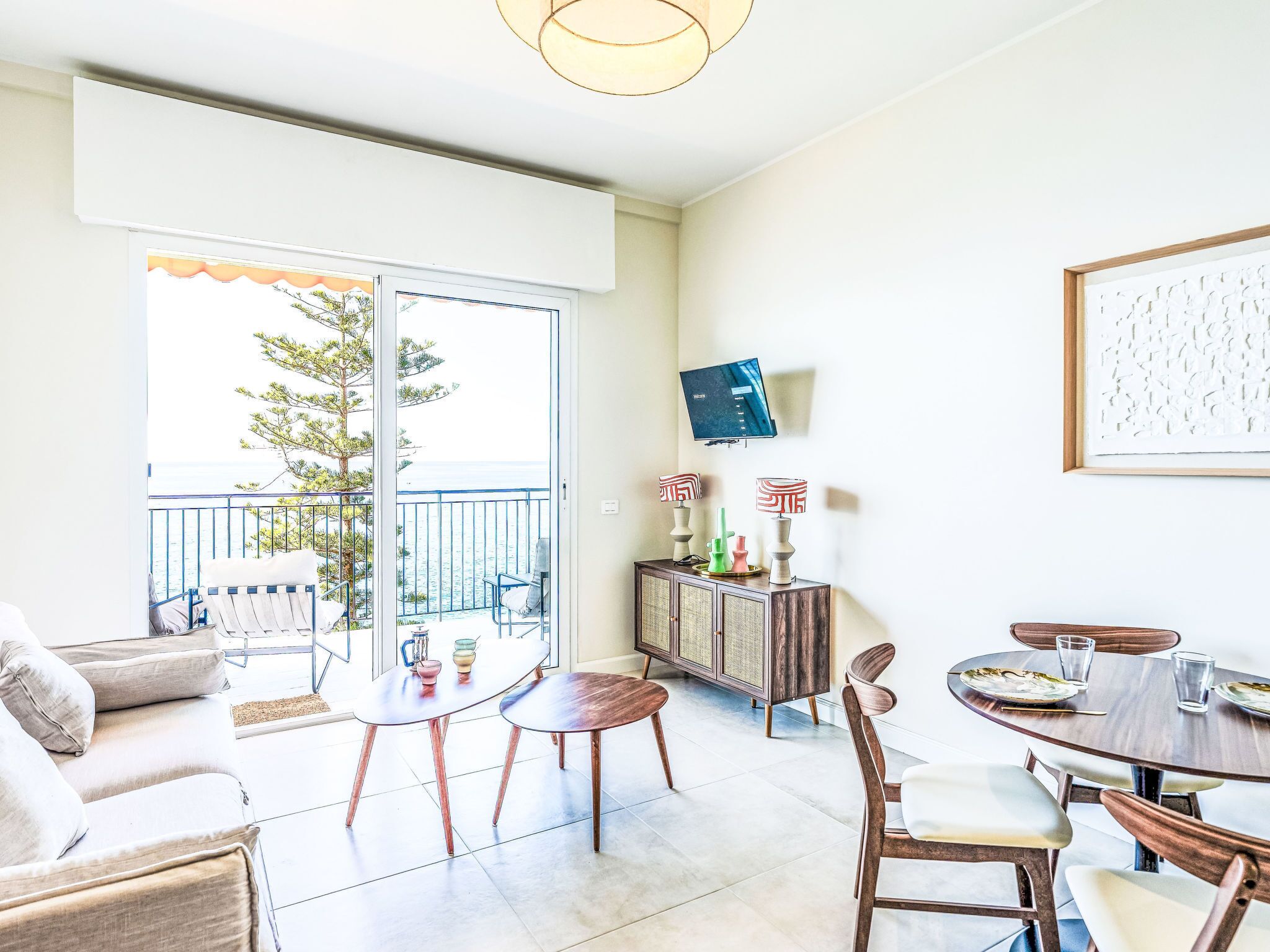 Un salon moderne avec balcon, un coin repas et un téléviseur fixé au mur.