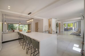 Eine moderne Küche mit einer großen Kücheninsel, Barhocker, Pendelleuchten und Blick ins Freie.