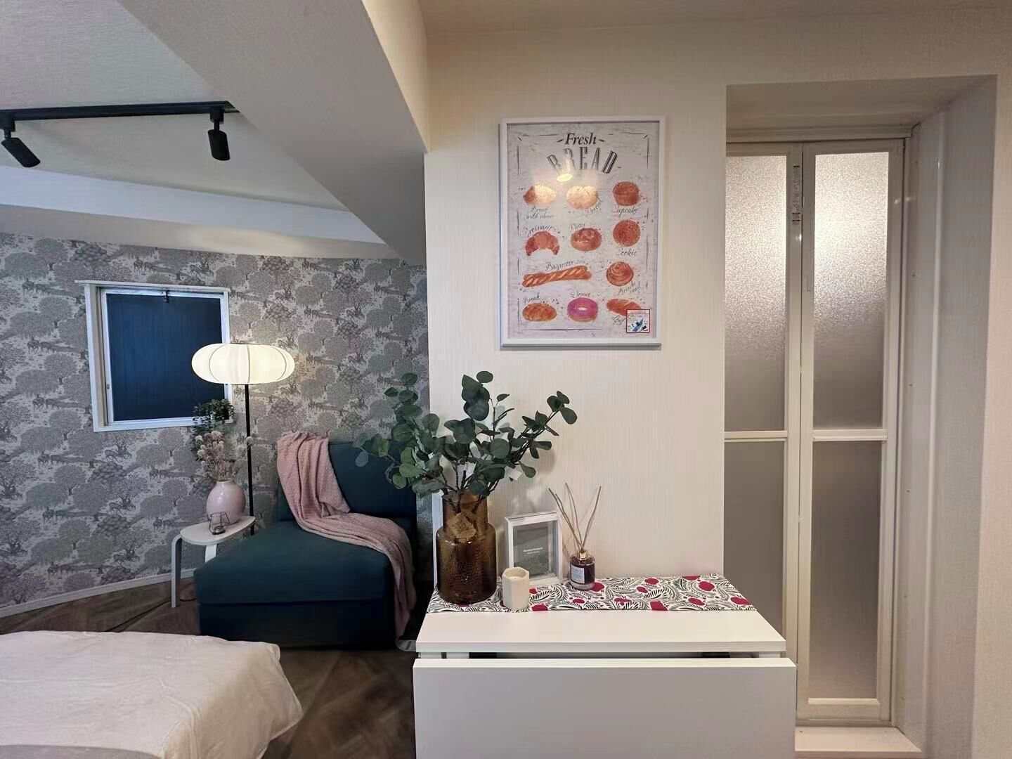 A modern bedroom with a stone-patterned wall, a bed, a desk with a vase and a lamp, and a poster of bread types.