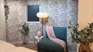 Ein modernes Schlafzimmer mit einem grünen Sofa, einem kleinen Nachttisch, einer Lampe und einem Fenster.
