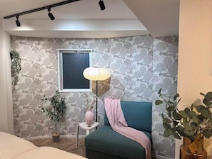 Ein modernes Schlafzimmer mit einem grünen Sofa, einem kleinen Nachttisch, einer Lampe und einem Fenster.