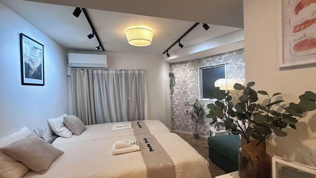 Ein Hotelzimmer mit einem Bett, einem Schreibtisch, einem Blumentopf, einem Fenster und einer Wand-Klimaanlage.