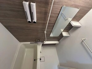 Ein modernes Badezimmer mit Holzboden, einer weißen Badewanne, einem Spiegel und zwei weißen Seifenspendern.