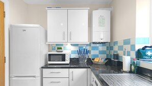 A compact kitchen with white cabinets, a microwave, a water dispenser, and a sink. - Heathrow Living Apt  01 by 360 Stays (Stanwell)