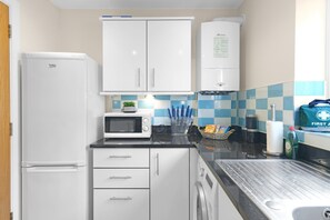 Una cocina compacta con armarios blancos, un microondas, un dispensador de agua y un lavabo.