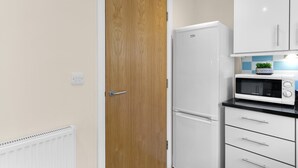 Eine Küche mit einem weißen Kühlschrank, einer Mikrowelle und einer Holztür.