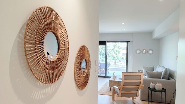 Una sala de estar moderna con un espejo redondo grande, una silla de madera, un sofá y una pequeña mesa con jarrones.