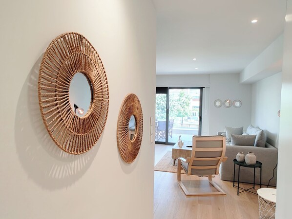 A modern living room with a large round mirror, a wooden chair, a sofa, and a small table with vases. - Boutique Riviera Stay in Voula Center (Voula)