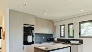 Una cocina moderna con una isla central, taburetes de bar, horno empotrado y ventana con vistas.