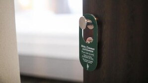 A door with a metal handle and a green sign with text in multiple languages. - Hotel Allee 55 (Hannover)