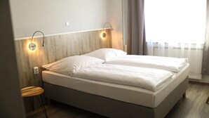 A single bed with a wooden headboard, two wall-mounted lights, a small wooden stool, and a window with curtains. - Hotel Allee 55 (Hannover)