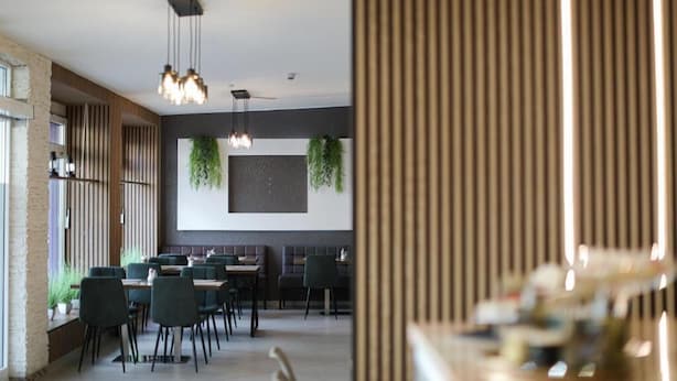 A modern restaurant with high tables and chairs, pendant lighting, and vertical wooden slats on the walls. - Hotel Allee 55 (Hannover)