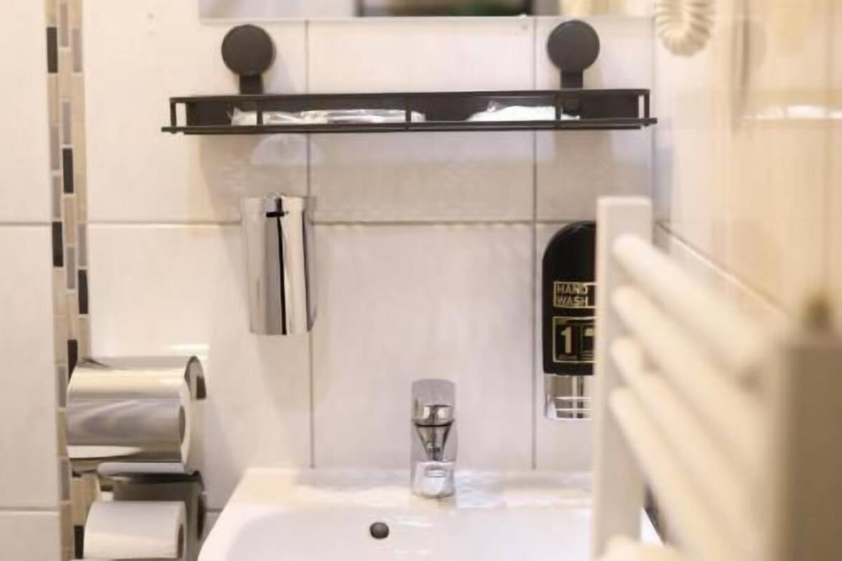 Un baño con lavamanos, perchero para toallas y dispensador de papel higiénico.
