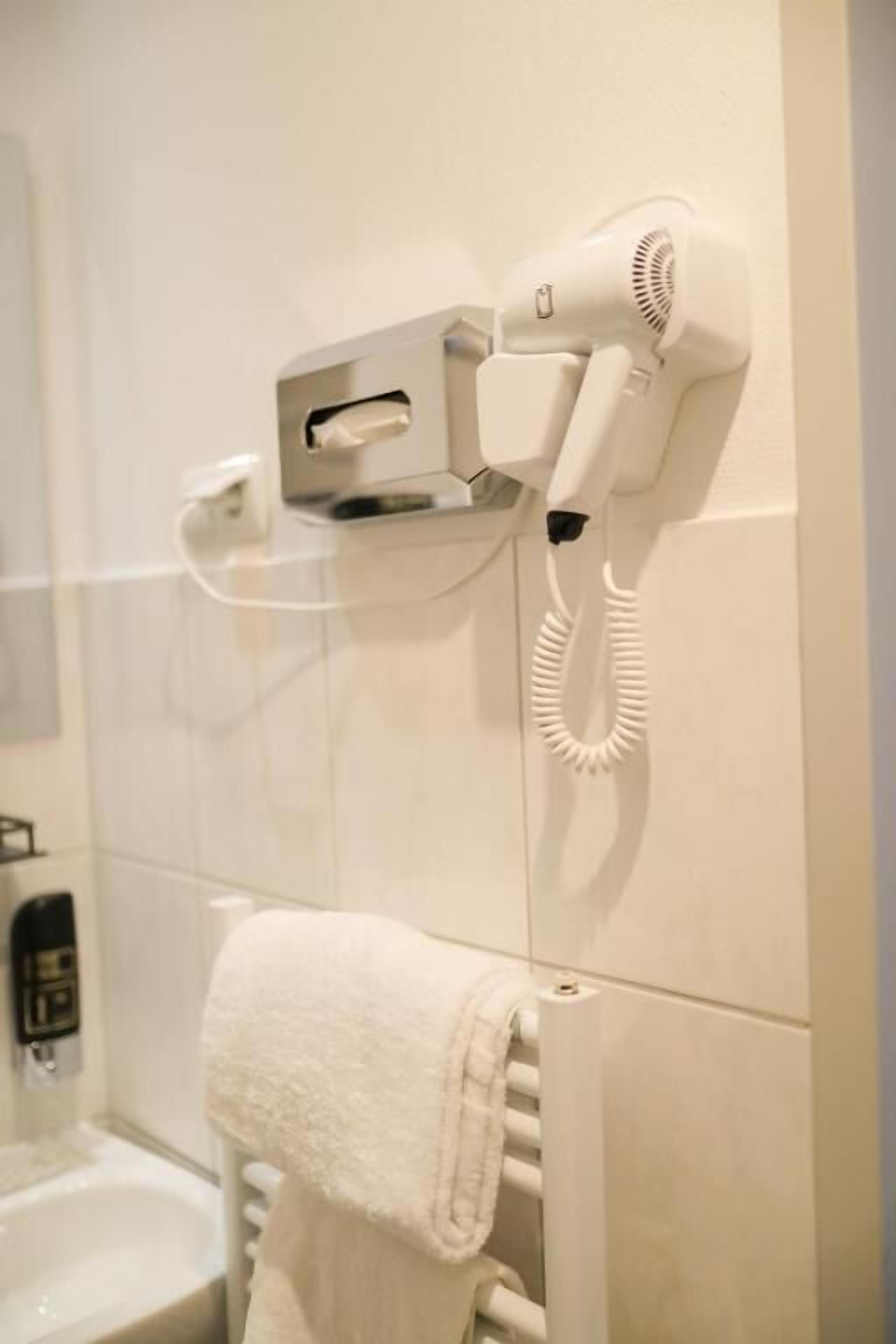 A bathroom with a hairdryer mounted on the wall, a towel rack with a towel, and a sink with a soap dispenser.