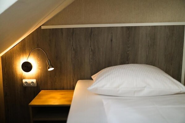 A bedroom with a wooden headboard, a bedside table, a lamp, and a bed with a pillow. - Hotel Allee 55 (Hannover)