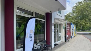 A hotel entrance with a banner, outdoor seating, and a clear view of the street. - Hotel Allee 55 (Hannover)