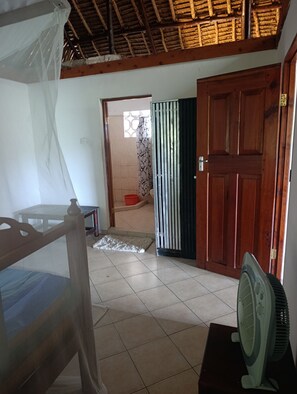 Ein Zimmer mit einem Bett, einem Ventilator, einer Tür und Blick auf ein weiteres Zimmer.