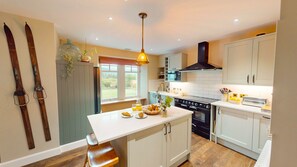 A kitchen with a central island, a stove, oven, and a window with a view of greenery.