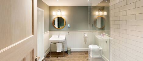 A bathroom with a wooden floor, a white sink, a toilet, and a glass-enclosed shower area.
