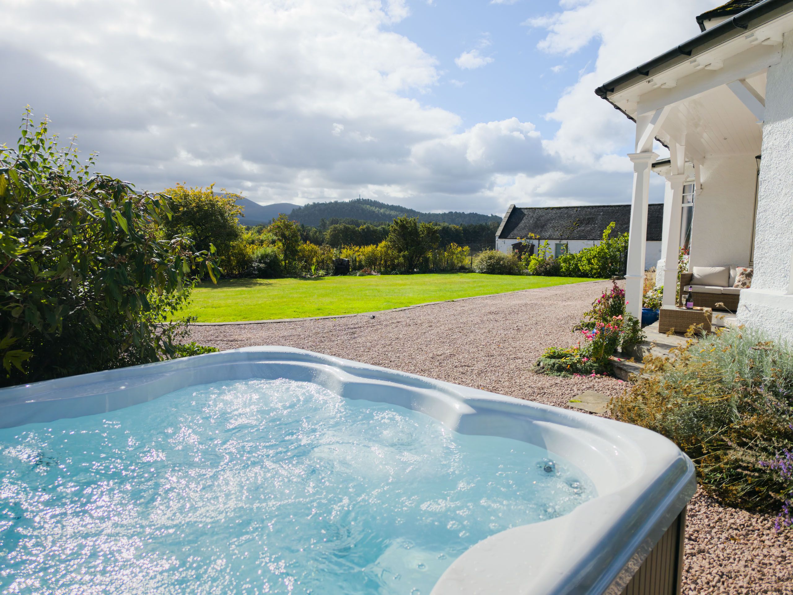 A hot tub in a garden with a house and mountains in the background.