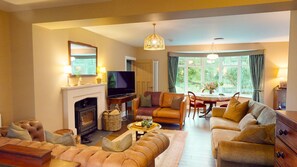 A living room with a fireplace, sofa, television, and dining area with a view of the outdoors.