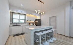 A modern kitchen with white cabinetry, a marble island, and bar stools. - Konmek Poolvilla (Sattahip)