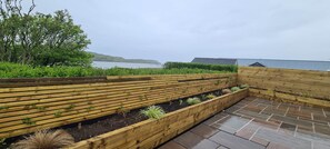 A wooden deck with raised planters, a stone patio, and a view of the sea.