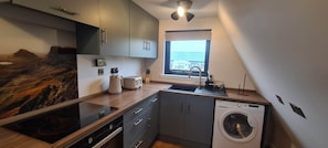 A compact kitchen with a built-in stove, a washing machine, and a window with a view of a building.