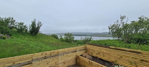 A wooden bench overlooking a lake with a grassy hillside and trees.