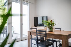 A modern dining area with a wooden table, black chairs, a TV, and a potted plant. - Apt Imola Autodromo with Terrace and Parking (Imola)