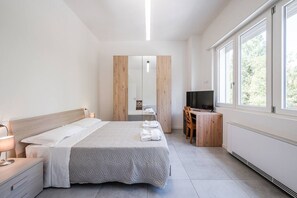 Una camera da letto moderna con un letto, comodino, televisione e ampie finestre.