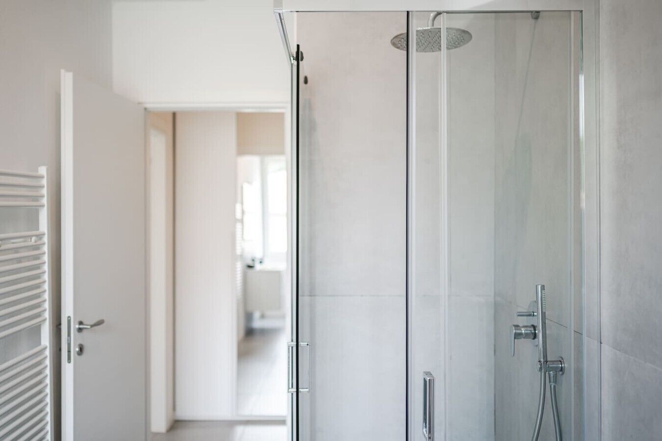 Ein modernes Badezimmer mit Duschkabine aus Glas, sichtbarer Toilette und einer Tür zu einem anderen Raum.
