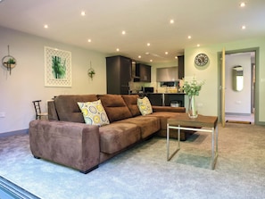 Ein Wohnzimmer mit einem braunen Ecksofa, einem kleinen Tisch und einer Pflanzvase.