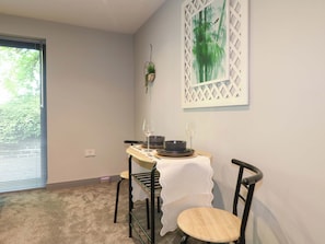 A dining area with a table set for two, a window with blinds, and a wall-mounted plant.
