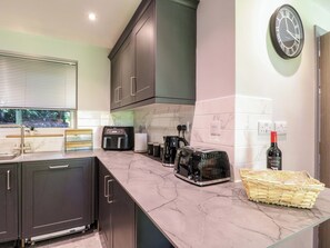 A modern kitchen with dark cabinets, a marble countertop, a coffee maker, a toaster, and a wine bottle. - Elmcroft (Nottingham)