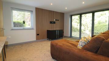 A modern living room with a sofa, a TV, a wooden panel wall, and large windows.