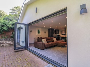 Ein modernes Haus mit Glastür, die in einen Wohnbereich mit einem braunen Ecksofa und einem Esstisch führt.