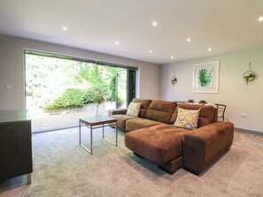 Ein modernes Wohnzimmer mit einem Ecksofa, einem Glastisch und Blick auf Grünfläche.