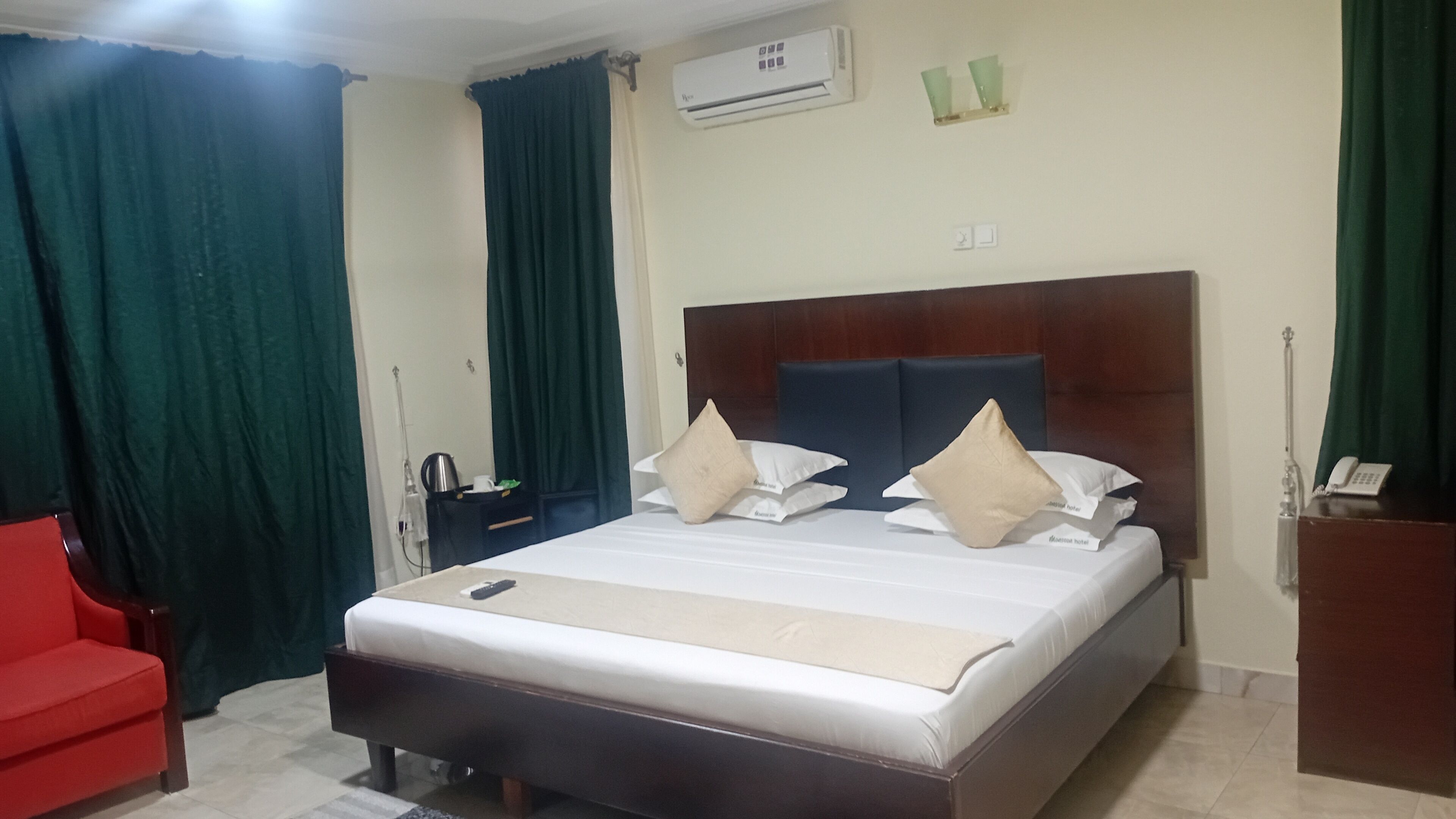 Una habitación de hotel con una cama, una silla roja, una mesita de noche y un equipo de aire acondicionado.