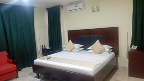 Una habitación de hotel con una cama, una silla roja, una mesita de noche y un equipo de aire acondicionado.