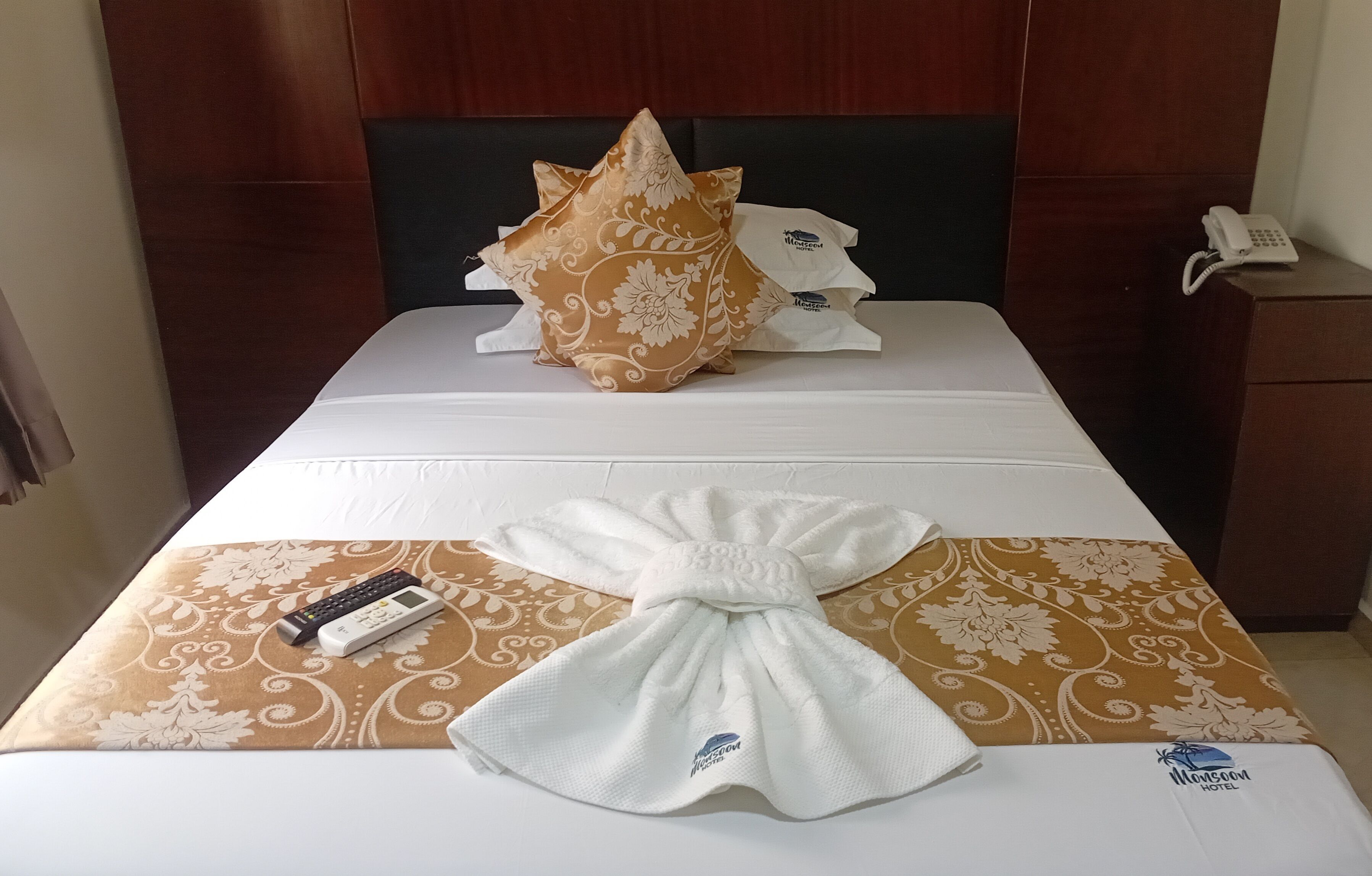 Una habitación de hotel con cama, almohada, toalla, control remoto y teléfono sobre una mesita de noche.