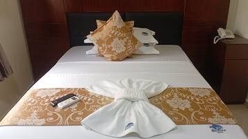 Una habitación de hotel con cama, almohada, toalla, control remoto y teléfono sobre una mesita de noche.
