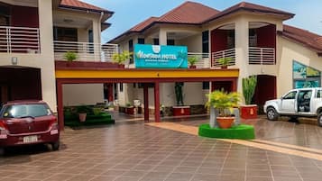 Un hotel con un letrero llamativo, un acceso cubierto y un estacionamiento con dos autos.