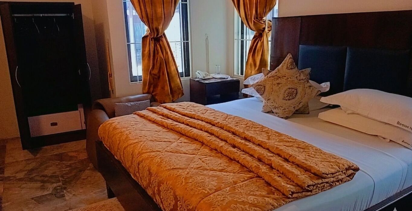 Une chambre d’hôtel avec un lit, une table de chevet, une armoire et une fenêtre avec des rideaux.