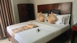 A hotel room with a bed, a wooden headboard, a brown patterned throw, and a remote control on the bed. - Monsoon Hotel Ltd (Kumasi)