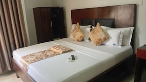 A hotel room with a bed, a wooden headboard, a brown patterned throw, and a remote control on the bed. - Monsoon Hotel Ltd (Kumasi)