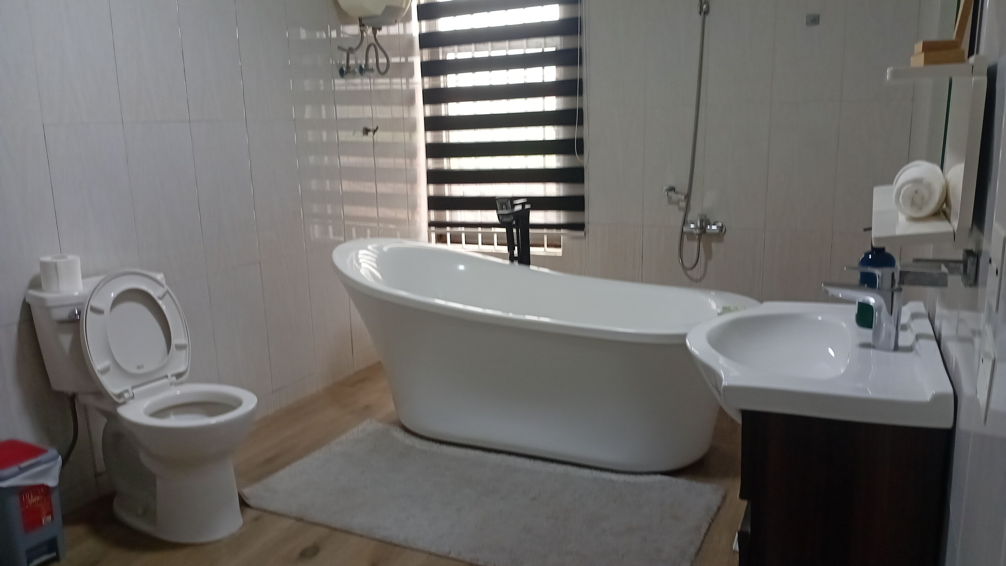 Un baño con inodoro, bañera, lavabo y ventana con persianas.