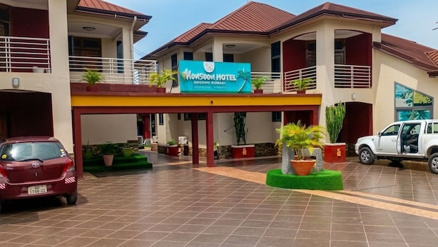 A hotel with a signboard, a covered entrance, potted plants, and a car parked in front. - Monsoon Hotel Ltd (Kumasi)