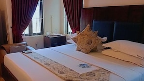 A hotel room with a bed, a nightstand, a lamp, and a window with curtains. - Monsoon Hotel Ltd (Kumasi)